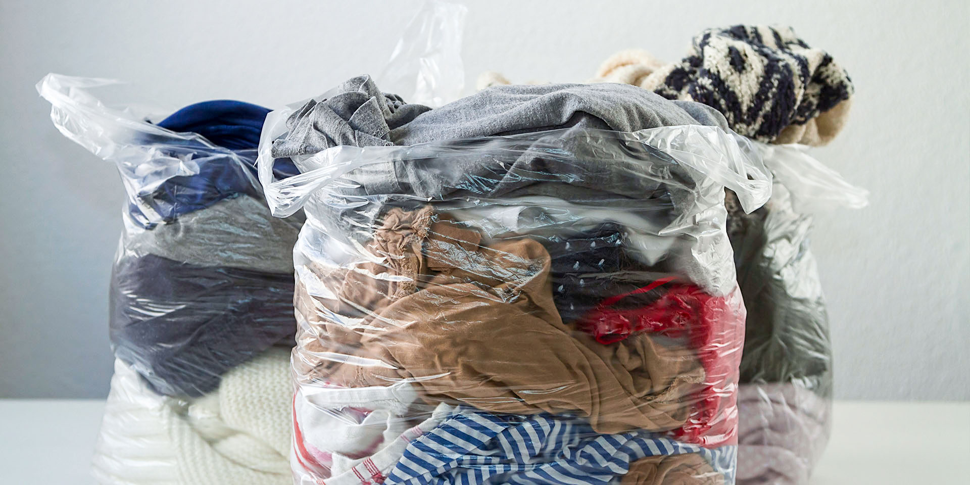 Three large clear plastic bags filled with sorted clothes and textiles sitting on a table.