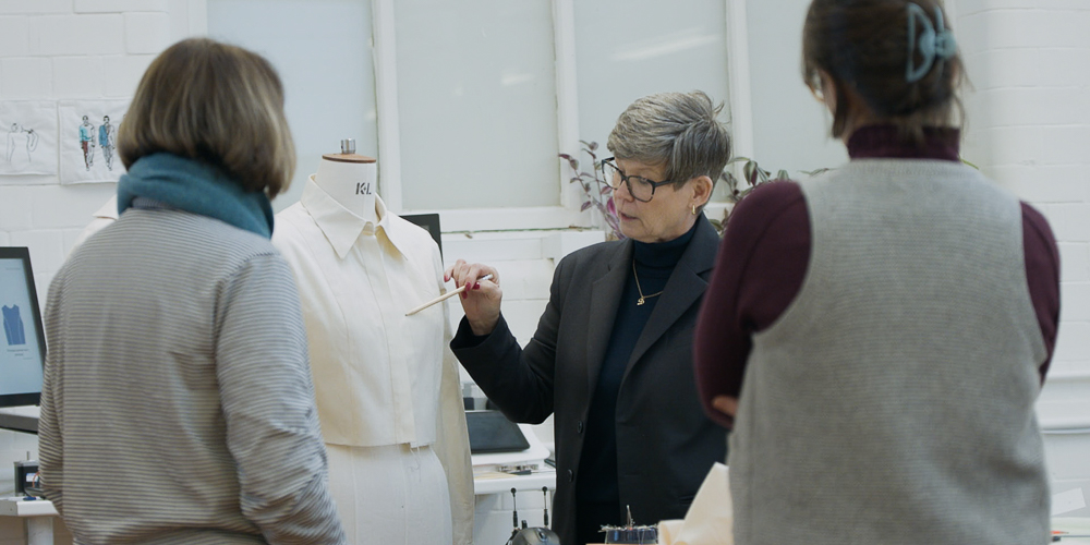 An instructor demonstrating garment fitting and pattern analysis on a mannequin to students in a studio setting.