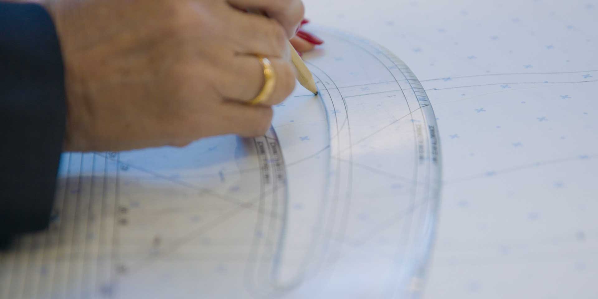 A fashion student or designer measuring and cutting paper garment patterns on a studio workbench.