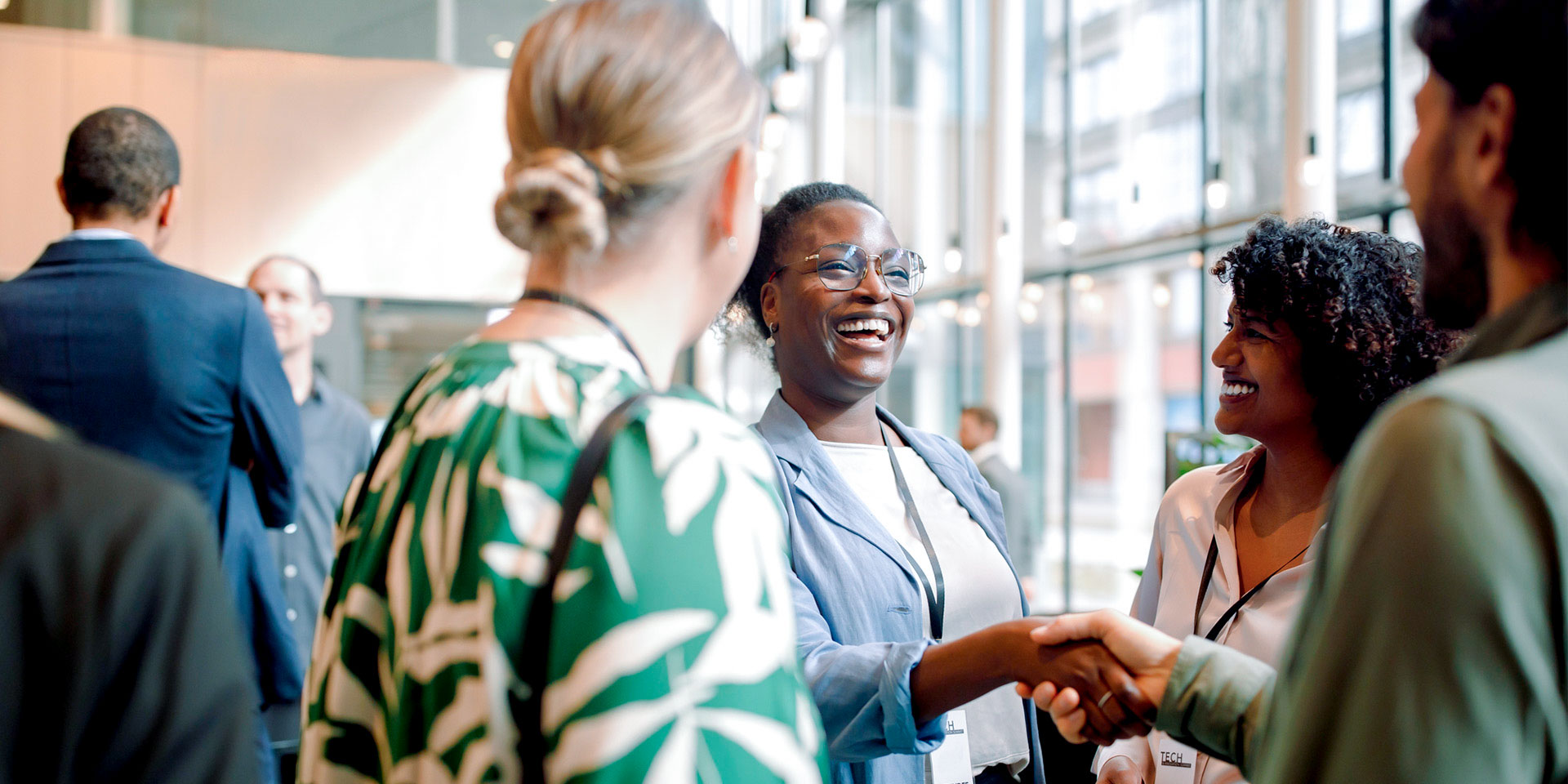 Professional attendees smiling and shaking hands at a networking event.