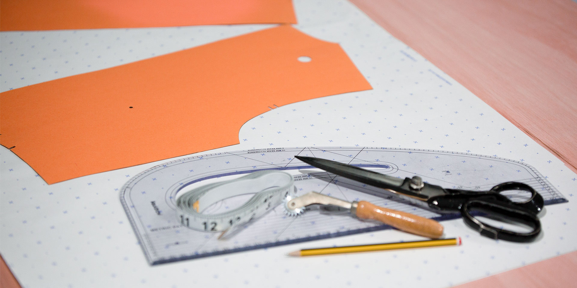 Pattern drafting supplies—including scissors, a curved ruler, tape measure, tracing wheel, and pencil—layout on pattern paper.
