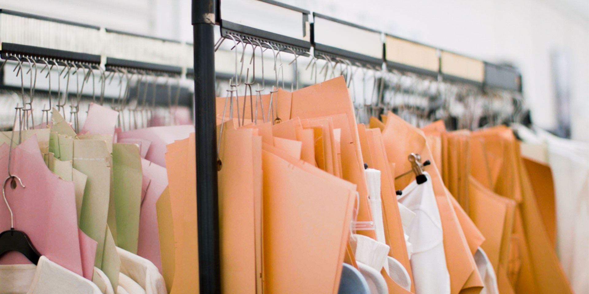 Paper garment patterns in various colors hanging organized on a metal clothing rack.