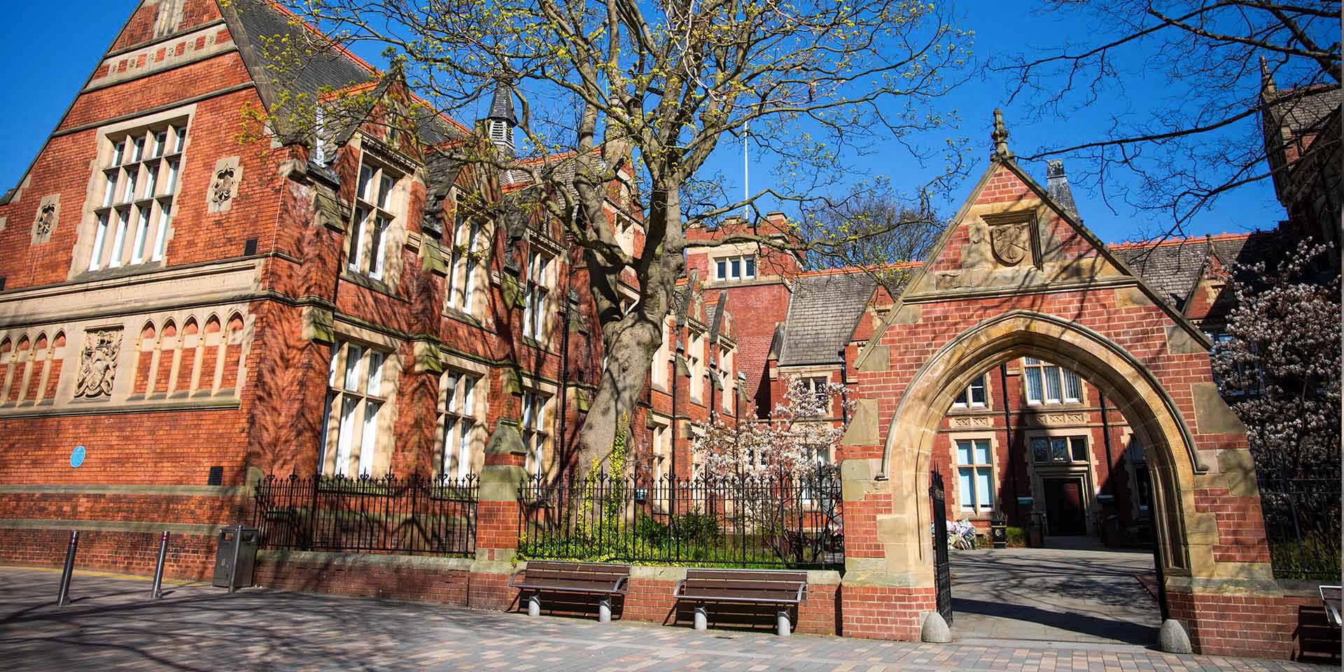 Exterior view of a red brick historical campus building with an archway under a sunny sky.