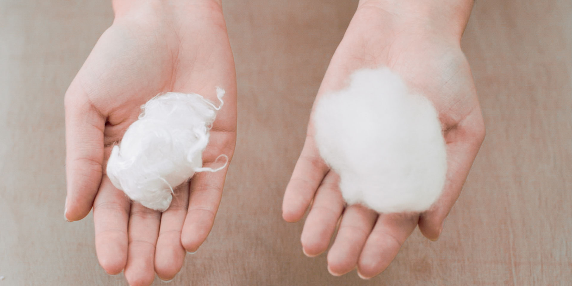 Two open hands displaying and comparing two different clumps of raw white textile fibers.